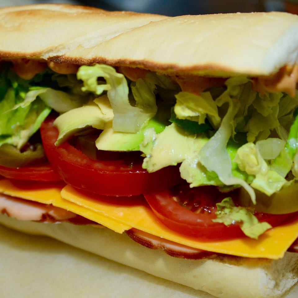 Close-up of a Sutter Street Cafe sandwich with lettuce, avocado, tomatoes, cheese, and meat.