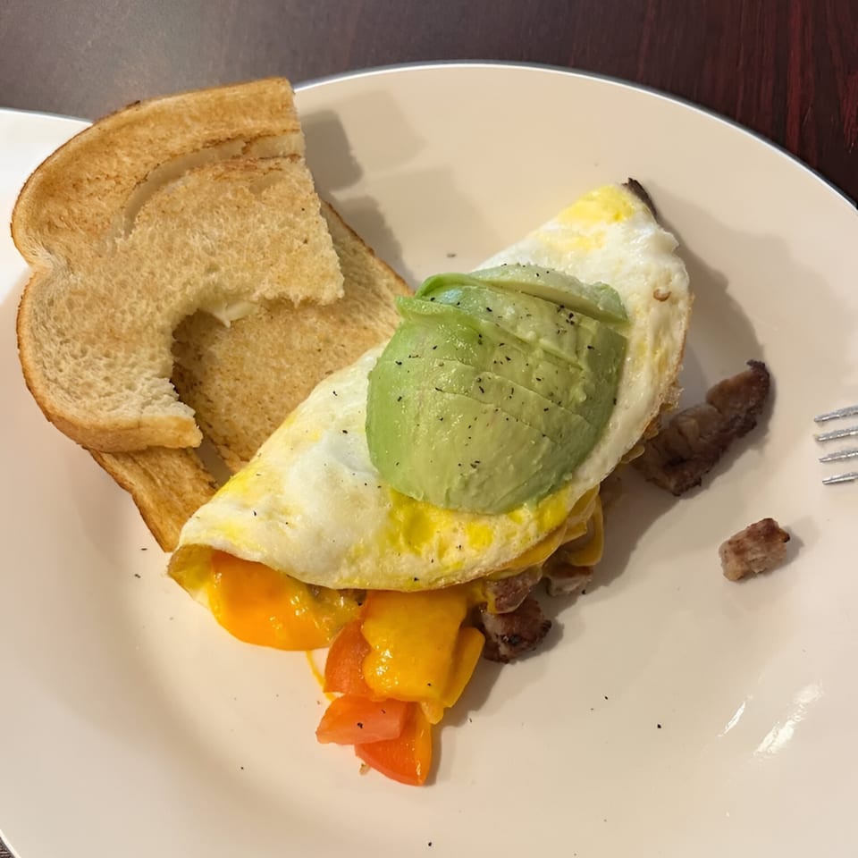 A Sutter Street Cafe breakfast plate with an omelet topped with avocado, toast, and bacon.