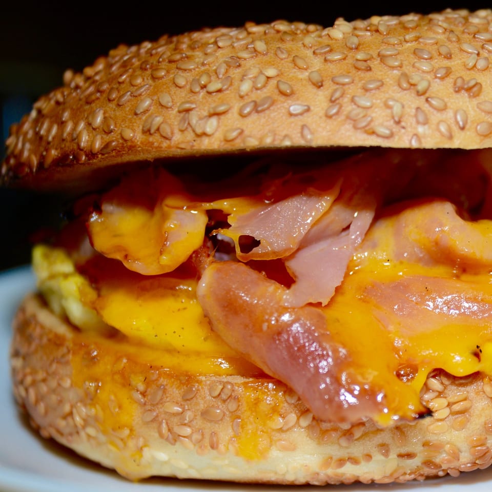 Close-up of a sesame bagel sandwich with melted cheese, ham, and scrambled egg.