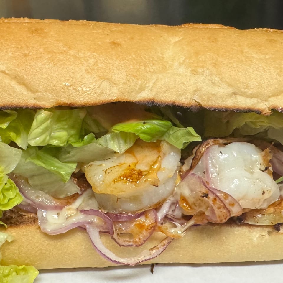 Close-up of a Sutter Street Cafe shrimp po'boy sandwich with lettuce, red onion, and sauce.