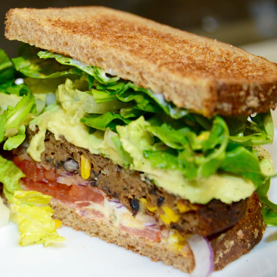 A Sutter Street Cafe veggie burger on toasted bread with lettuce, tomato, onion, and avocado.