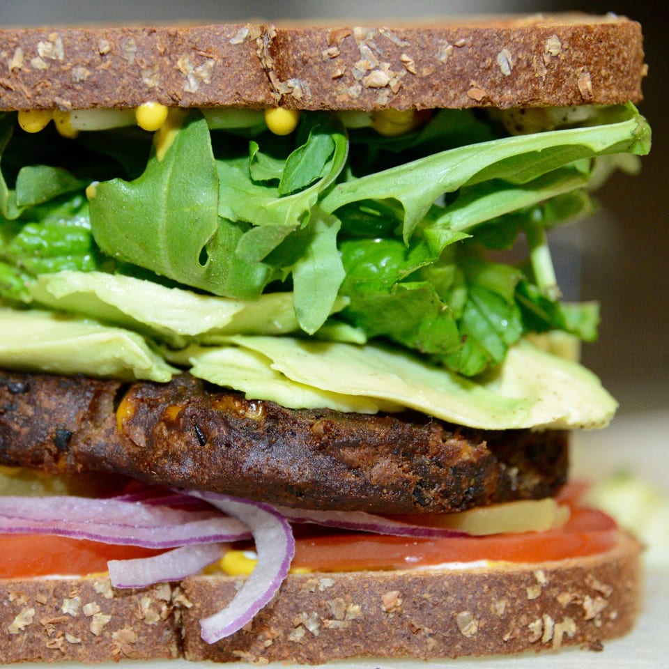 Close-up of a Sutter Street Cafe veggie burger on wheat bread with avocado, lettuce, tomato, and onion.