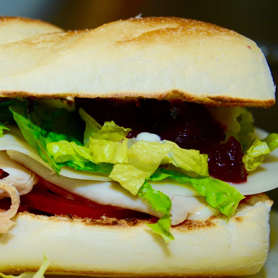 Close-up of a Sutter Street Cafe sandwich with turkey, cheese, lettuce, tomato, and cranberry sauce.
