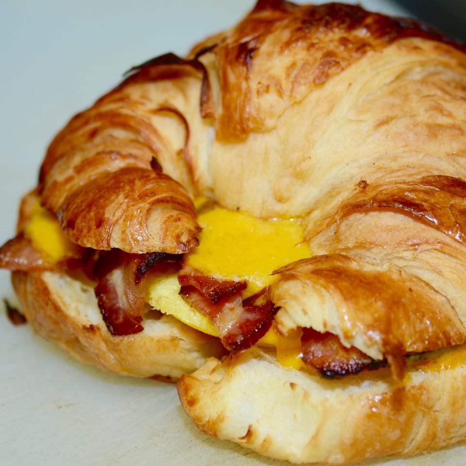 Close-up of a Sutter Street Cafe croissant breakfast sandwich with bacon, egg, and cheese.
