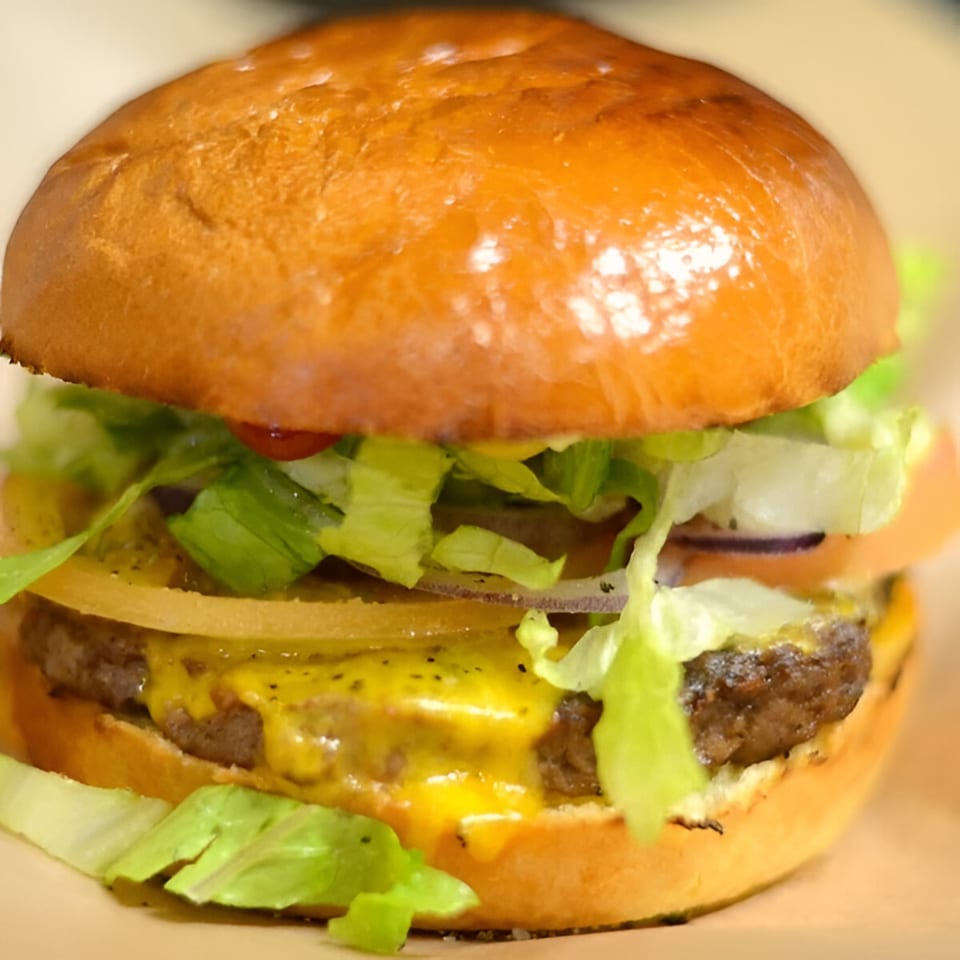 A Sutter Street Cafe burger with melted cheese, lettuce, onions, and tomato on a brioche bun.